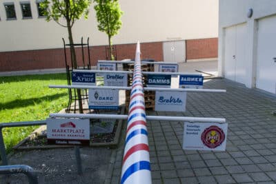 Maibaum, am Boden liegend, mit Logos der Sponsoren.