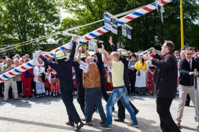 Eine Gruppe Männer, bestehend aus Feuerwehrleute und zivil gekleidete Personen, beim Aufstellen des Maibaums. Rechts im Bild in einer braunen Jacke der 2. Vorsitzender des Vereins Olaf Böttger
